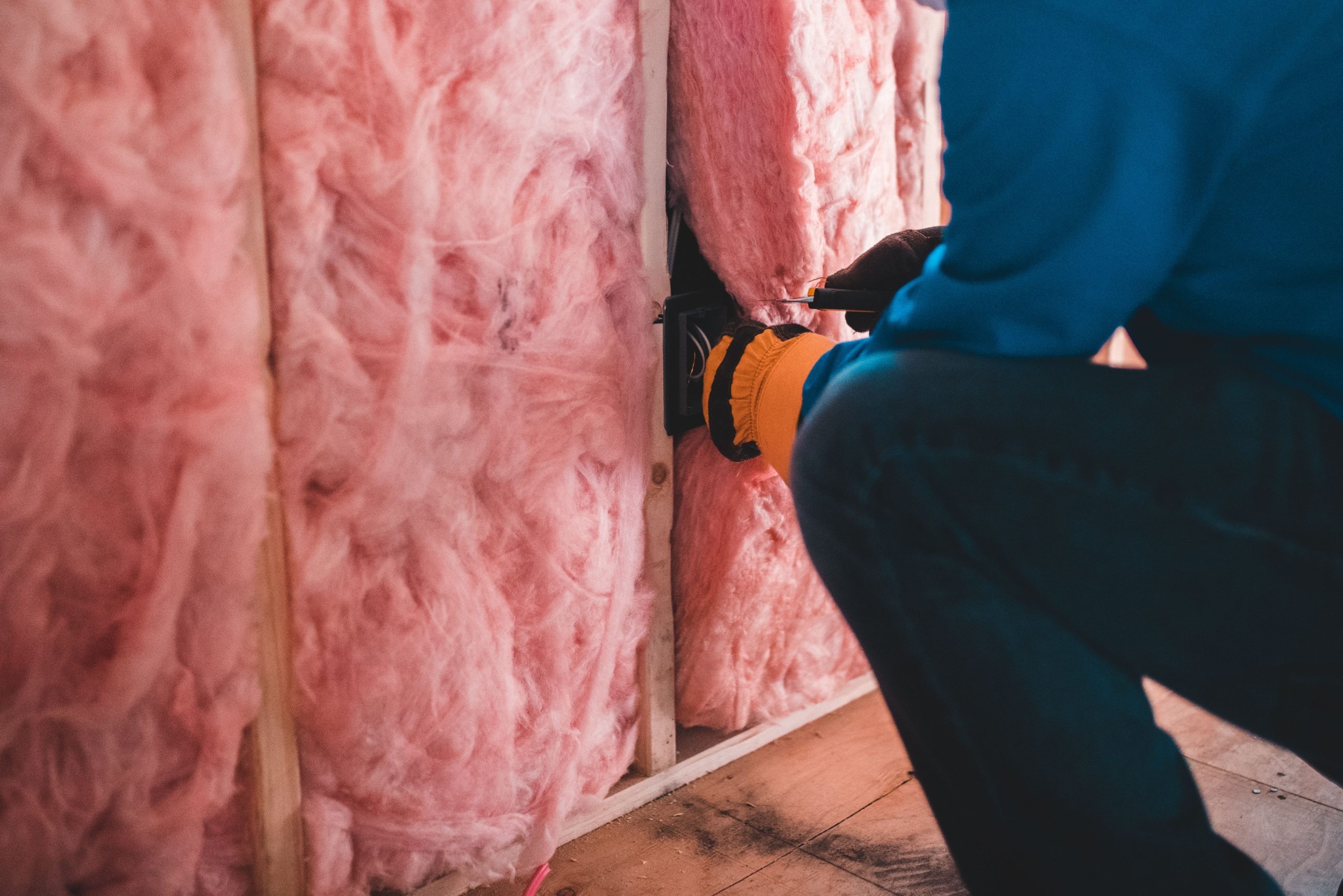 Ouvrier posant de la laine de verre entre les montants d'une ossature, travaux d'isolation thermique